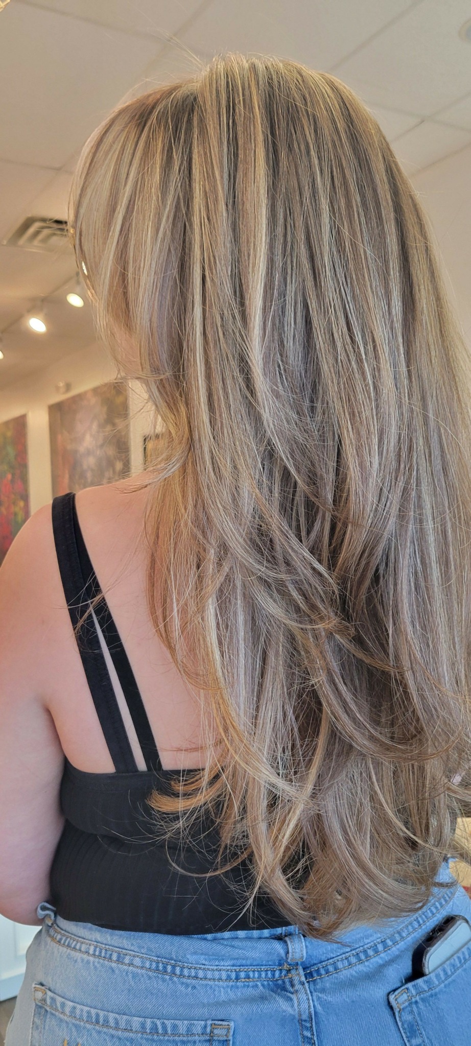 Person with long, wavy blonde hair wearing a black top and blue denim jacket.