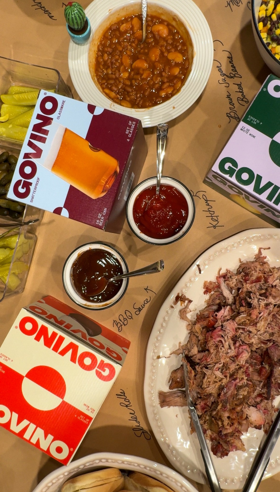 Table with bowls of soup, meat, and sauces, along with boxes of Govino disposable drinkware, on a brown paper tablecloth.