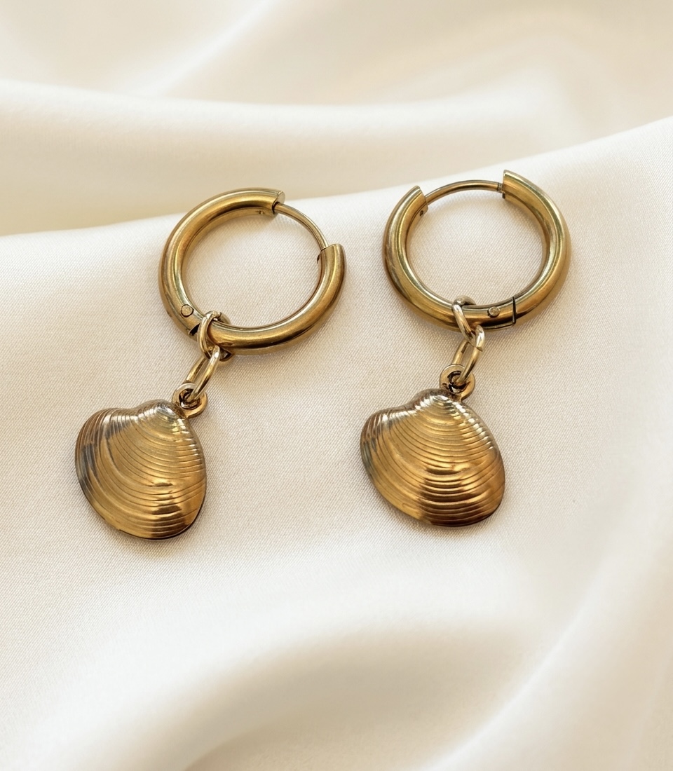 Pair of gold hoop earrings with shell-shaped pendants on white fabric, close-up view.