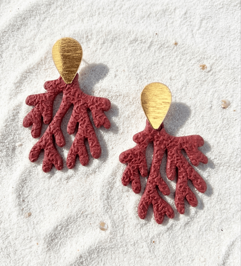 Red coral-shaped earrings with gold hooks on a textured white surface.