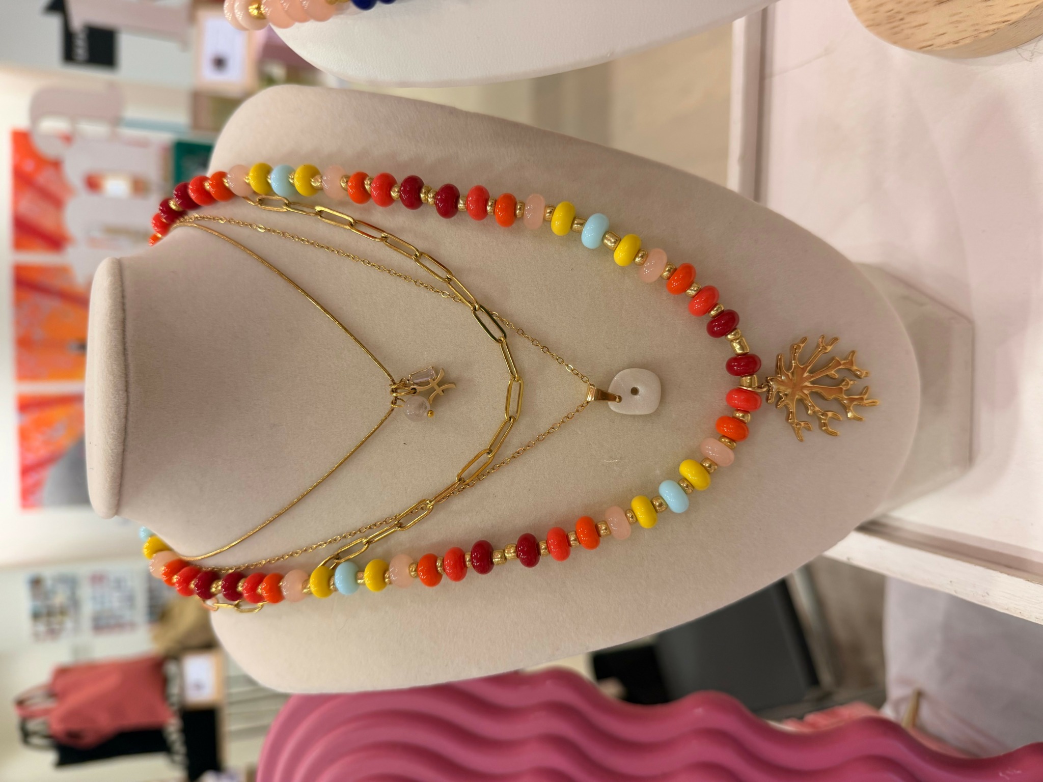 Jewelry display with layered necklaces and a beaded necklace on a white bust, with a blurred background of store interior.
