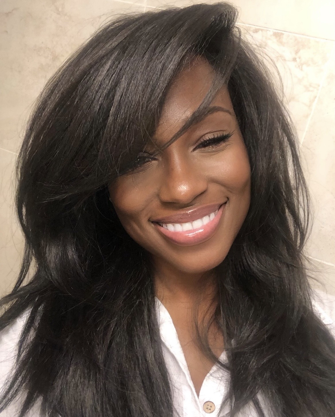 Smiling woman with long, dark hair and closed eyes, wearing a white shirt, in a neutral background.
