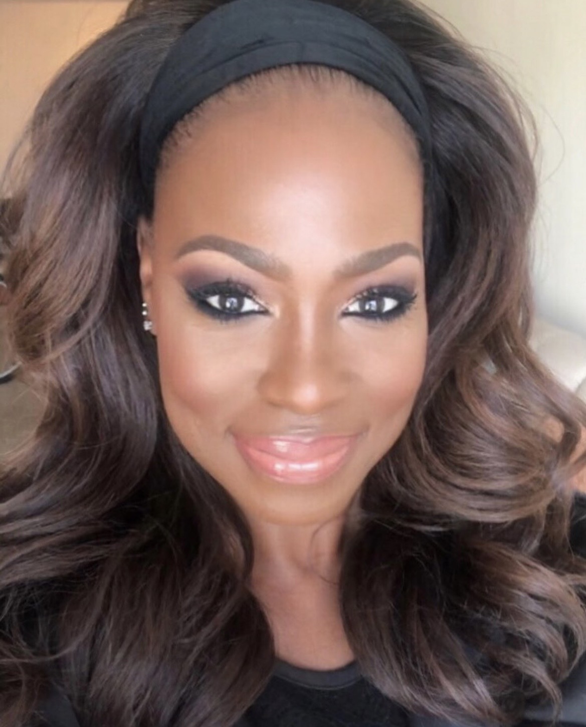 Close-up of a woman with styled hair, makeup, and a headband, smiling at the camera.